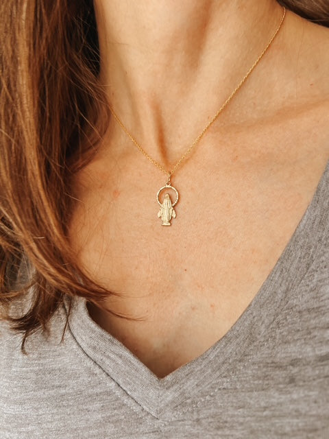 A close-up of a woman's neck a wearing a delicate gold pendant Miraculous Medal with an open halo of stars.
